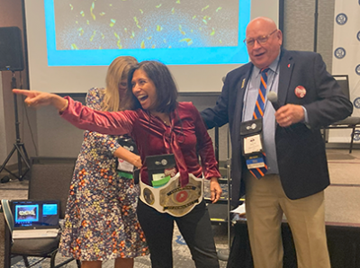 Outgoing NNA Chair John Galer, (right) publisher of The Journal-News, Hillsboro, Illinois, passes the gavel over to incoming NNA Chair Martha Diaz-Aszkenazy, publisher of the San Fernando (California) Valley Sun. She puts on a fighting victory belt, courtesy of NNA member Timothy Linscott, 
publisher, Fairbury (Nebraska) Journal-News. Click here to view photos/download.